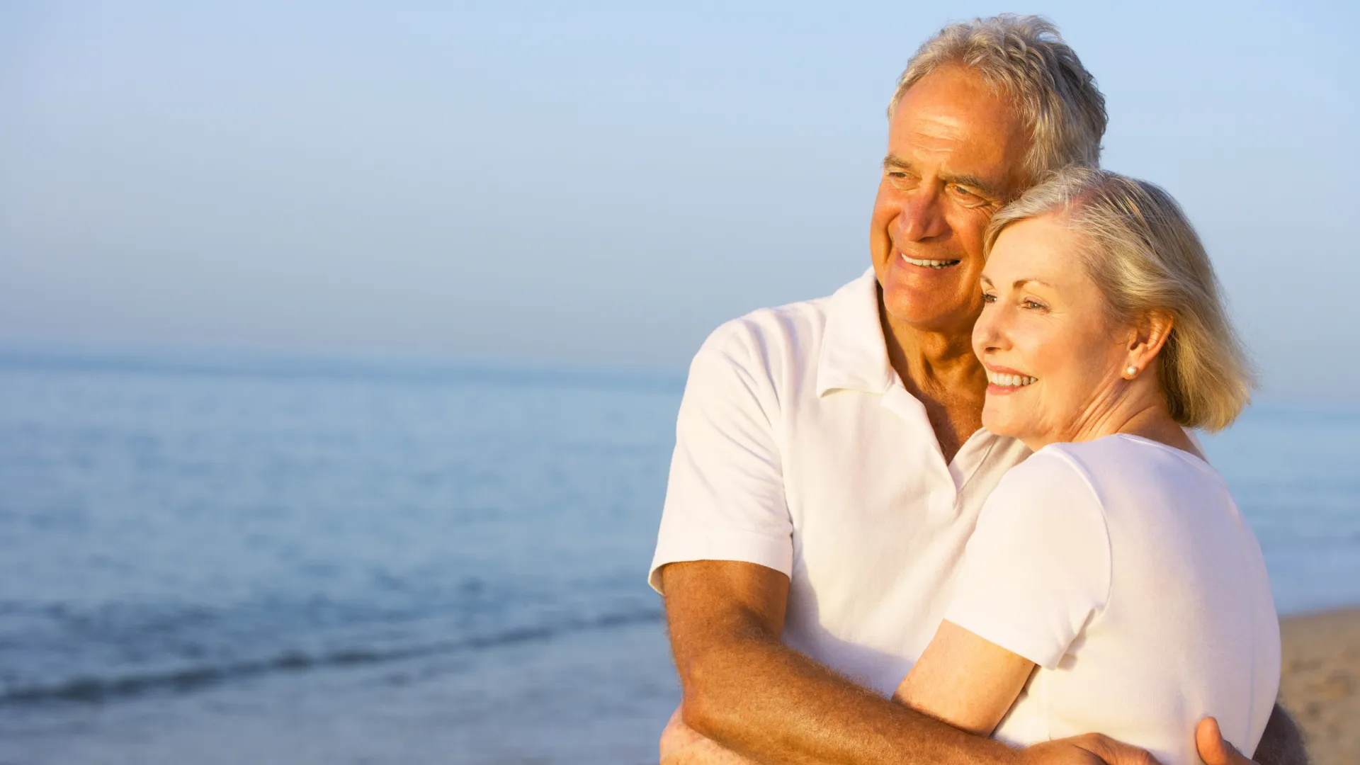 Older couple smiling on a beach waves in the background